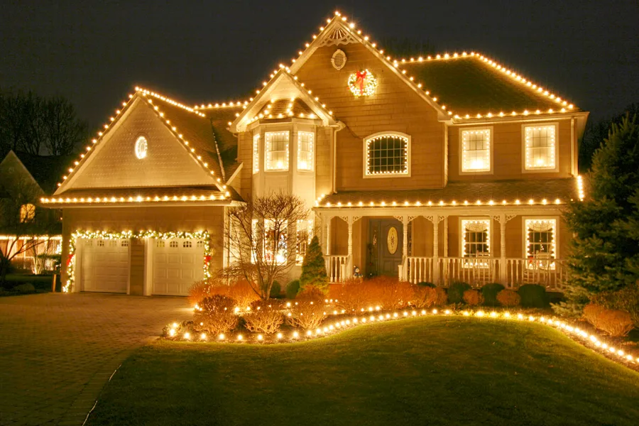 Warm white holiday lighting on a home's roof, shrubs and walkway