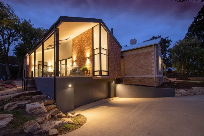 Uplighting washing a home facade at dusk with a lit driveway and walkway